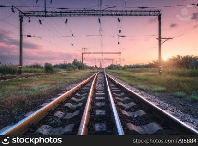 Railroad and pink sky at sunset. Summer rural industrial landscape with railway station, sky with colorful clouds and sunlight, green grass. Beautiful railway platform. Freight transportation. Cargo. Railroad and pink sky at sunset in summer. Industrial landscape
