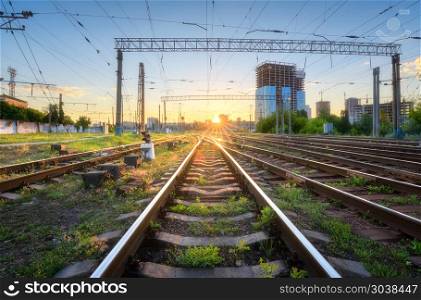 Railroad at beautiful sunset in Europe. Industrial landscape with railway station, green grass, buildings, blue sky with sun. Railway junction in the evening. Railway platfform. Transportation. . Industrial landscape with railway station, green grass, buildings