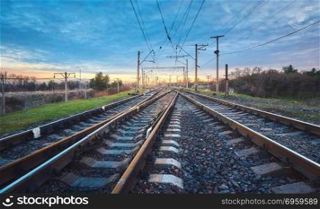 Railroad at sunset. Railway station against blue sky. Industrial landscape with railroad, cloudy sky, green grass, trees. Railway junction. Heavy industry. Cargo shipping. Freight transoprtation. Railroad at beautiful sunset. Railway station
