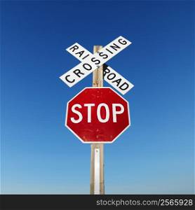 Railroad crossing and stop signs against blue sky.
