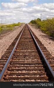 Railroad tracks lead off into the distance under a beautiful Teaxs Sky