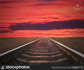 rails going away into the crimson sunset. rails going away into the crimson sunset. rails going away into the dark landscape with fiery red sunset