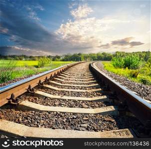 Railway in green field in the evening. The concept of moving forward, towards the goal. Railway in green field