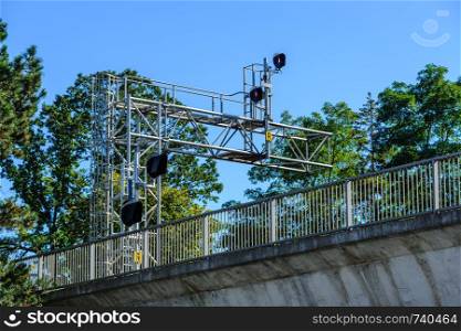 Railway signals and signs on metal frame among trees above bridge with fence.