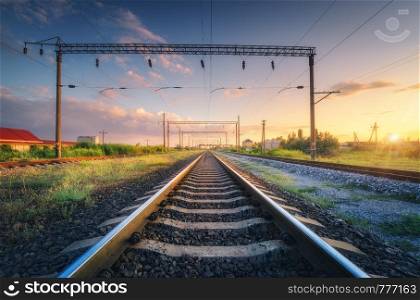 Railway station and beautiful sky at sunset. Summer rural industrial landscape with railroad, blue sky with colorful clouds and green grass at dusk. Railway junction. Transportation. Heavy industry
