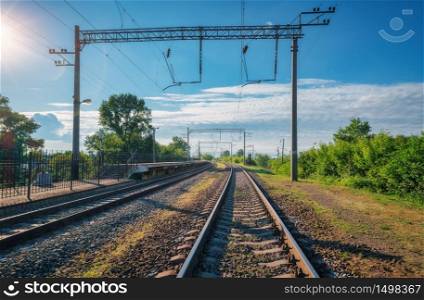 Railway station at bright sunny day in summer. Railroad in Europe. Heavy industry. Industrial landscape with railway platform, green trees, blue sky with clouds and sunlight. Transportation