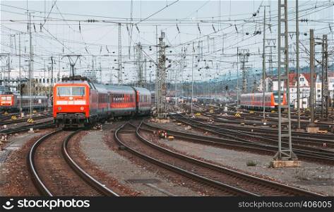 Railway station with modern red commuter train in motion in the evening in Nuremberg, Germany. Red train on the railroad track with vintage toning