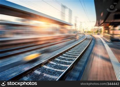 Railway station with motion blur effect at sunset. Industrial landscape with railroad, blurred railway platform, sky with orange sunlight in the evening. Railway junction in Europe. Transportation