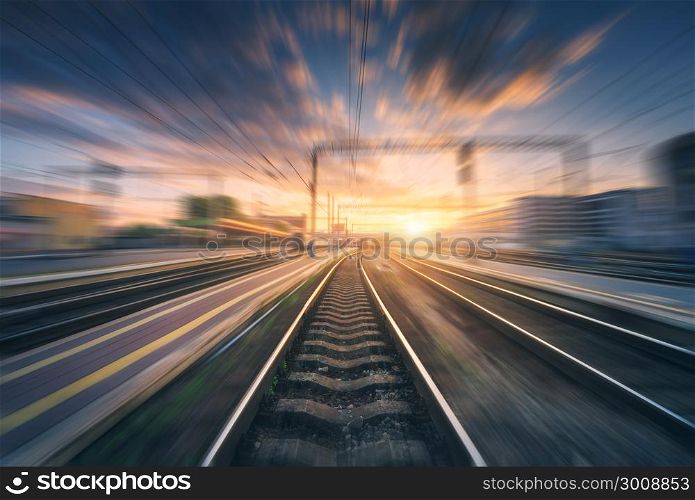 Railway station with motion blur effect. Blurred railroad. Industrial conceptual landscape with blurred railway station, buildings, blue sky with colorful clouds and sun. Railway track. Background. Railway station with motion blur effect. Blurred railroad