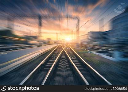 Railway station with motion blur effect. Blurred railroad. Industrial conceptual landscape with blurred railway station, buildings, blue sky with colorful clouds and sun. Railway track. Background. Railway station with motion blur effect. Blurred railroad