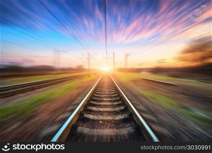 Railway station with motion blur effect. Blurred railroad. Railway station with motion blur effect at sunset. Blurred railroad. Industrial conceptual landscape with blurred railway station, blue sky with pink clouds and sunlight. Railway track in summer