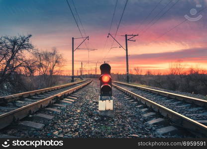 Railway station with semaphore against sunny sky with clouds at sunset. Colorful industrial landscape. Railroad. Railway platform with traffic light in the evening. Heavy industry. Cargo shipping. Railway station with traffic light at sunset