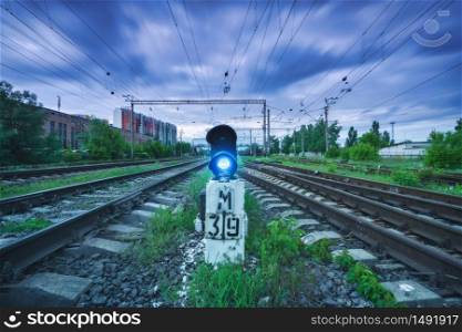 Railway station with traffic light and blurred sky with clouds at sunset. Dramatic industrial landscape with railroad. Railway platform with semaphore with blue light. Heavy industry. Transportation