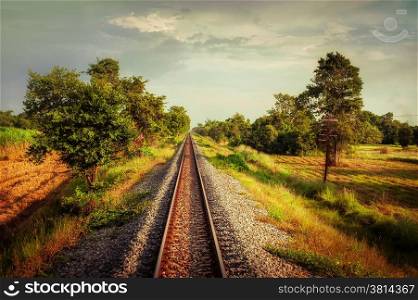 Railway track crossing rural landscape under evening sunset sky. Travel concept in vintage style