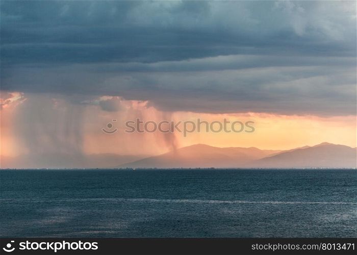 Rain clouds in distant plains near mountains. Rain pouring from clouds over distant plains near mountains with orange sun light at the horizon