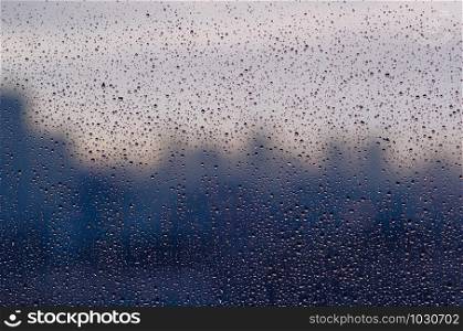 Rain drop on glass window in monsoon season with blurred city buildings background for abstract and background concept.