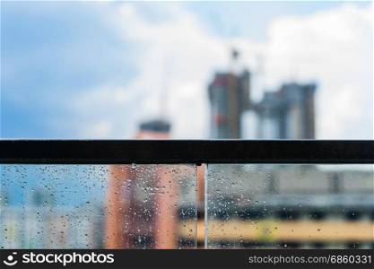 Rain drops on glass balcony, rainy day and construction in background with blue sky