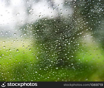 Rain drops on glass / Rainy day window glass with water drops and nature blur background