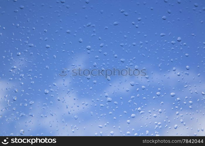 rain drops on window pane and blue sky with white clouds