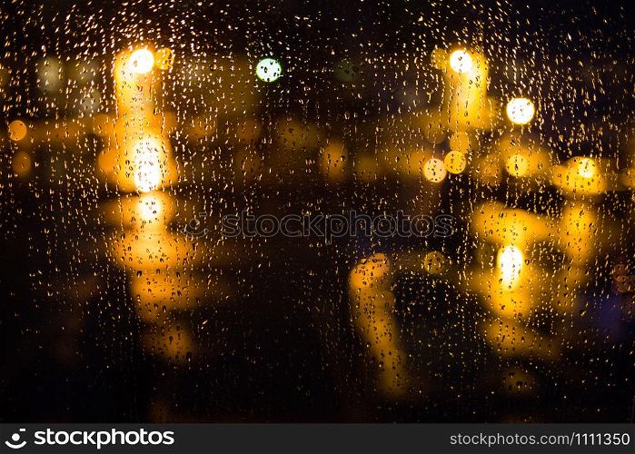 Rain drops on window. Peaceful evening or night at home when raining outside. Water drops on glass. Surface of wet glass. Water splash. City lights bokeh during the rain.. Rain drops on window. Peaceful evening at home