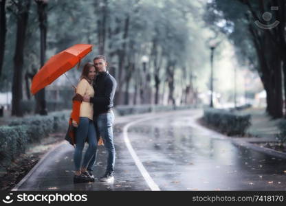 rain in the autumn park / young 25 years old couple man and woman walk under an umbrella in wet rainy weather, walk October lovers