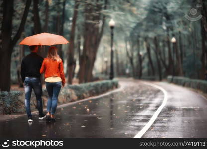 rain in the autumn park / young 25 years old couple man and woman walk under an umbrella in wet rainy weather, walk October lovers