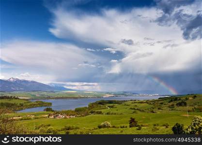 Rainbow after rain. Spring rain and storm in mountains. Green spring hills of Slovakia. Spring stormy scene. Clouds and sunny countryside.