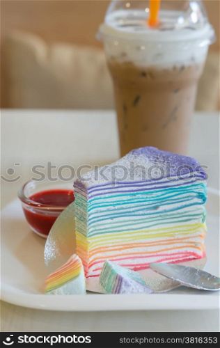 Rainbow crepe cake served with strawberry sauce and ice coffee. Rainbow crepe cake