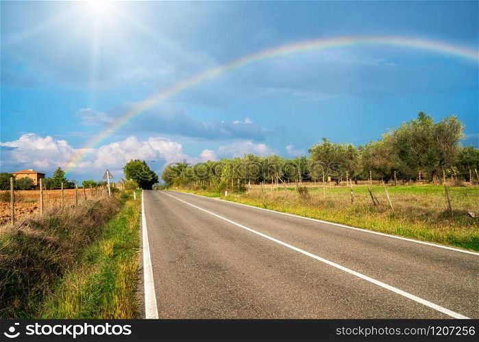 Rainbow over countryside highway road and agriculture landscape in Tuscany, Italy.. The rainbow over road and agriculture landscape.
