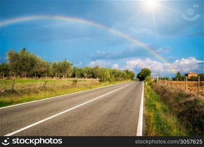 Rainbow over countryside highway road and agriculture landscape in Tuscany, Italy.. The rainbow over road and agriculture landscape.