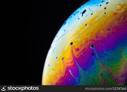 Rainbow soap bubble on a dark background. Close-up of colorful surface.. Abstract background made from soap bubble reflecting light