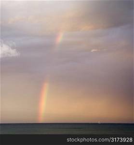 Rainbow spreading across sky on coast in Maui Hawaii.