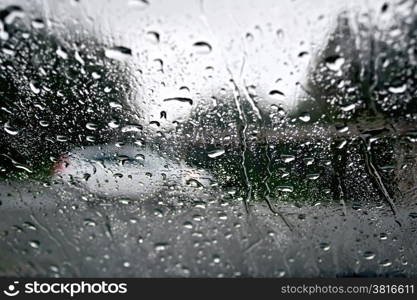 Raindrops on a glass window with blurry trees, road and white car