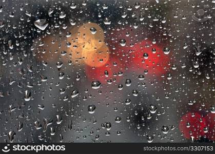 Raindrops on glass surface and blurry abstract city lights. Background texture.