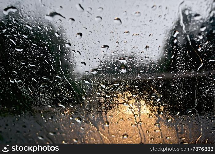 Raindrops on glass window with blurred trees, the road and the yellow lights of the car