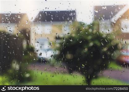 Raindrops on window glass in rainy day with blurry tree and house background, View looking trough window with water drops texture taken after the rain over road background