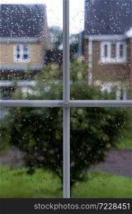Raindrops on window glass in rainy day with blurry tree and house background, View looking trough window frame with water drops texture taken after the rain over road background