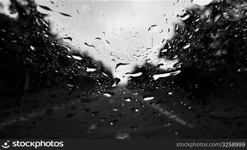 Raindrops on window with blurry road in background.