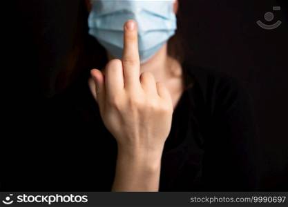 Raise the middle finger for Coronavirus, Female wearing protective medical mask for Covid-19 dark background, Concept for Corona and health, Stop Covid design. Raise the middle finger for Coronavirus, Female wearing protective medical mask for Covid-19 dark background, Concept for Corona and health, Stop Covid