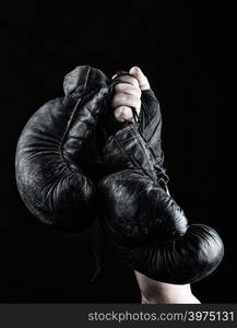 raised up man&rsquo;s hand holds a pair of old black leather boxing gloves, black background