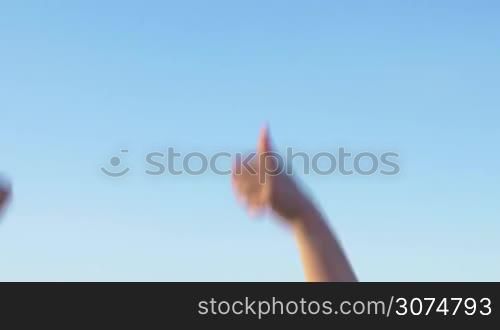 Raising hands with thumbs-up on clear blue sky background. People expressing agreement and support