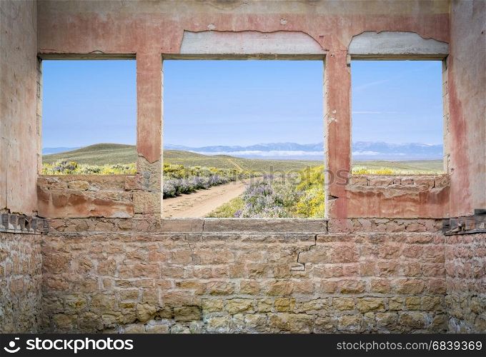 ranch road through mountain valley as seen through windows of an abandoned house