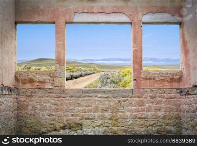 ranch road through mountain valley as seen through windows of an abandoned house