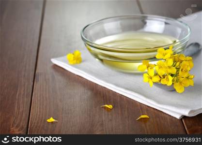 Rapeseed oil in bowl with flower of rapeseed. Food composition on wooden background