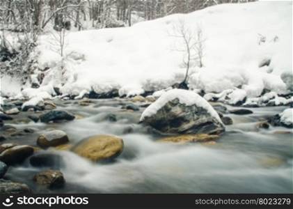 Rapidly flowing mountain river on a background of snow-covered forest, blurred by a slow shutter speed