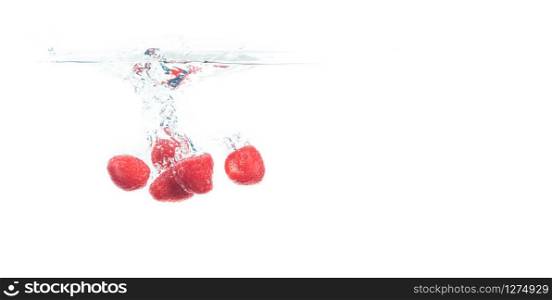 Raspberries falling into a water isolated on white background. Sinking under water with lots of air bubbles. Copy space on right. Blueberries falling into a water isolated on white background