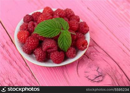 Raspberries in a bowl on a wooden table pink