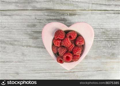 Raspberries in a bowl on wood. Heart shape bowl.