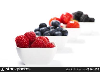 raspberries in front of wild berries in bowls. raspberries in front of wild berries in bowls on white background