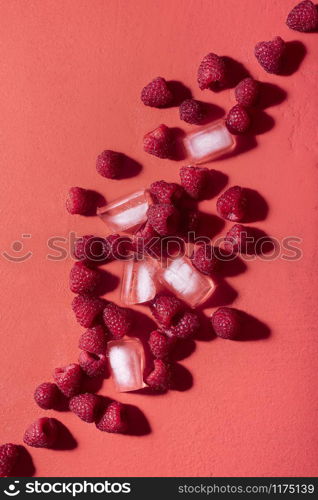 Raspberries pile and ice cubes scattered on a lush lava background in sunlight. Summer fruit cocktail ingredients. Fresh berries lemonade ingredients.